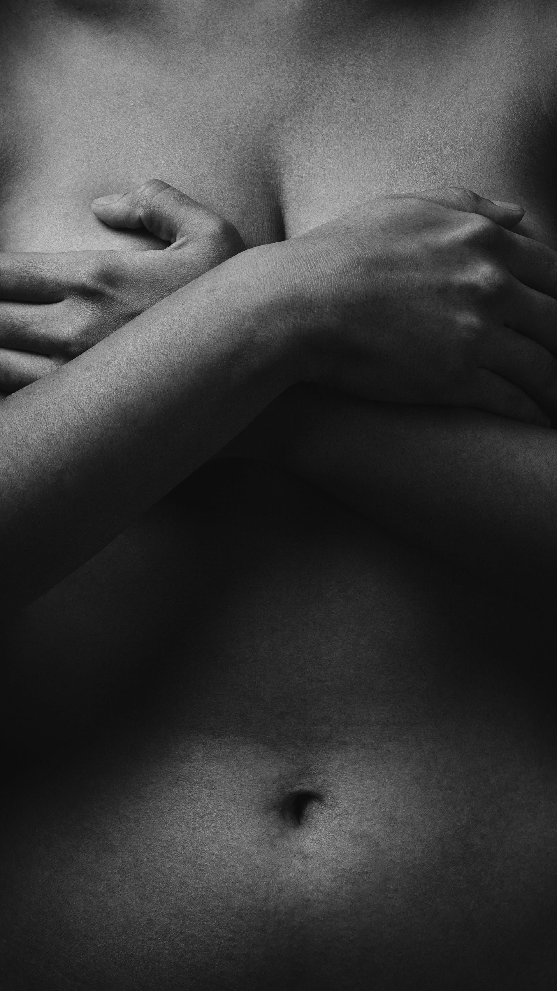 Buste de femme, en noir et blanc, dont les bras cachent la poitrine.
