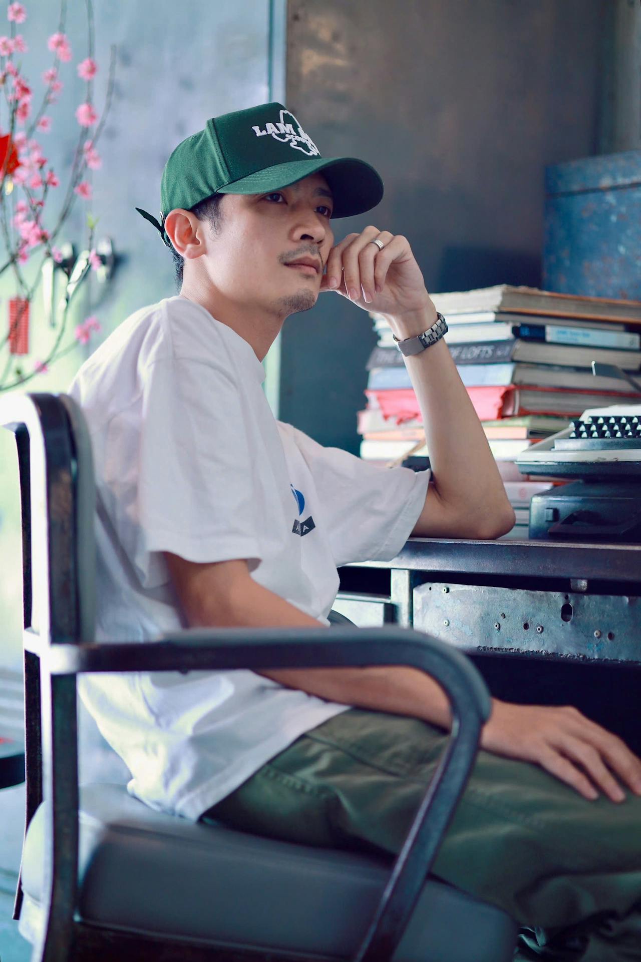 Un jeune homme assis sur son fauteuil et accoudé son bureau encombré de livres