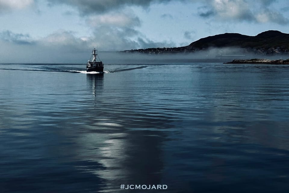 Un bateau sort d'un nuage de brume. Derrière lui, Saint-Pierre de Saint-Pierre-et-Miquelon.
