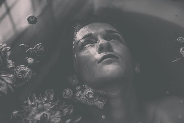 Visage d'un corps immergé dans un bain, fixant le plafond.