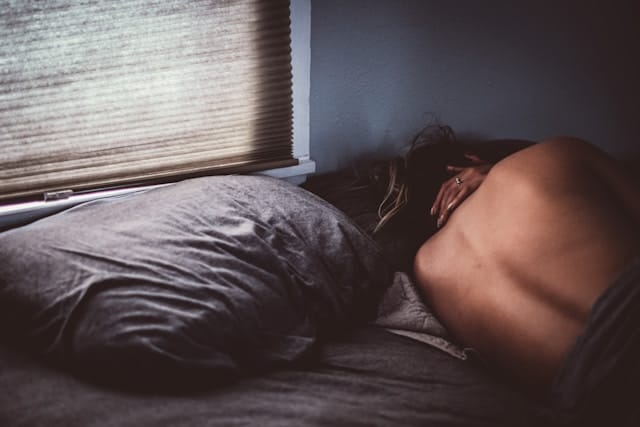 Femme endormie dans son lit, en tenue de peau, tournant le dos à l'observateur.