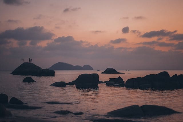 Deux silhouettes sur un rocher entouré d'eau.