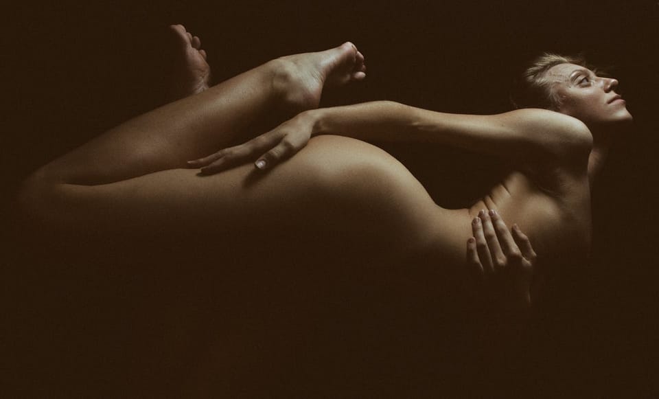Nu artistique en sépia chaud, femme courbée de profil se tenant la poitrine, une main sur une fesse, tête et pieds relevés comme pour se rejoindre.