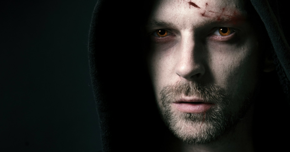 Un portrait d'homme encapuchonné qui présente une entaille légère au front. Ses yeux sont des couleur cuivre.