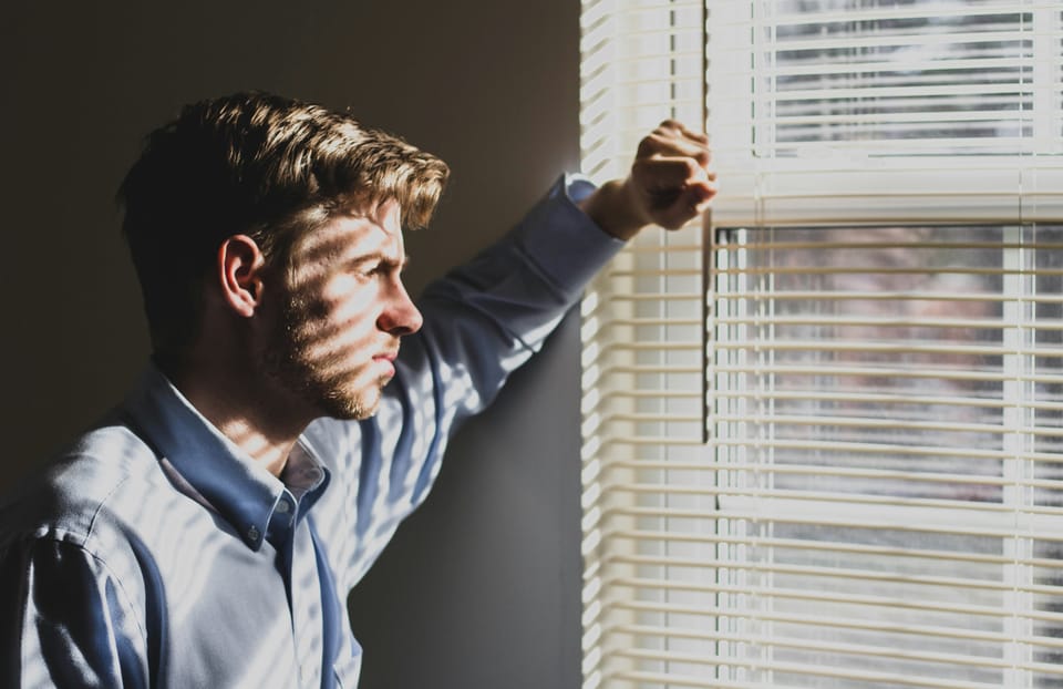 Un homme regarde avec nostalgie au travers de persiennes.