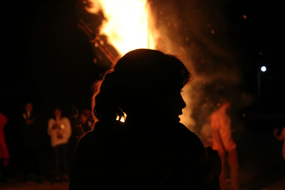 Une silhouette en avant plan, devant un brasier autour duquel sont réunies diverses personnes.