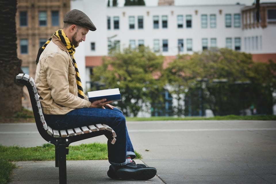 Un homme assis sur un banc, il lit un livre.