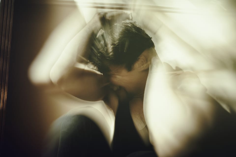 Un homme qui hurle intérieurement en se cachant entre ses bras. Double exposition.