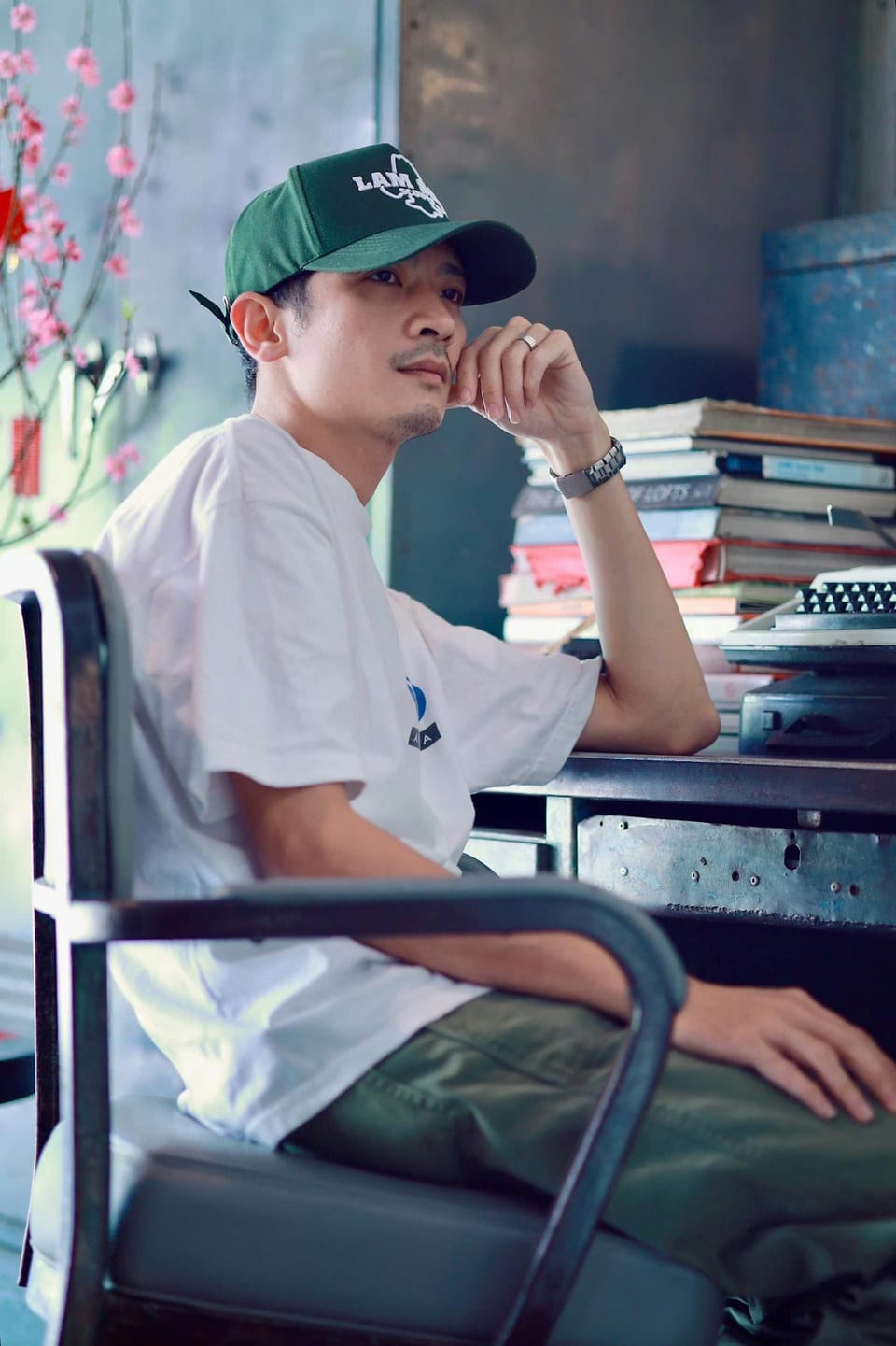 Un jeune homme assis sur son fauteuil et accoudé son bureau encombré de livres