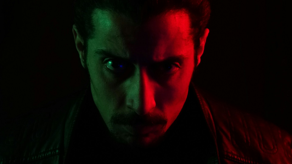 Portrait d'un homme en plan rapproché. Il est dans le noir, éclairé d'un côté par une lumière rouge.
